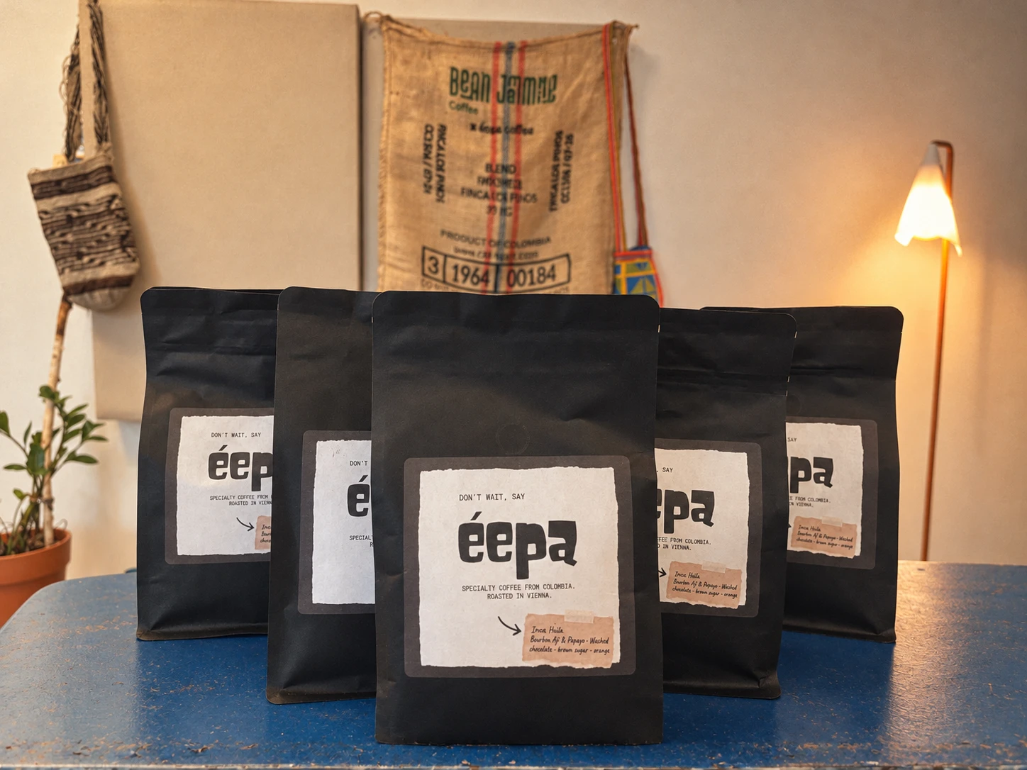 Five éepa coffee bags on a blue table, with a Bean Jamming coffee sack on the wall behind