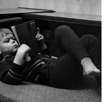 Black and white photo of a child lying down, reading a book