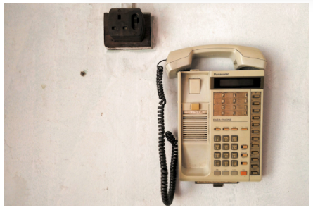 Old beige office telephone mounted on a white wall